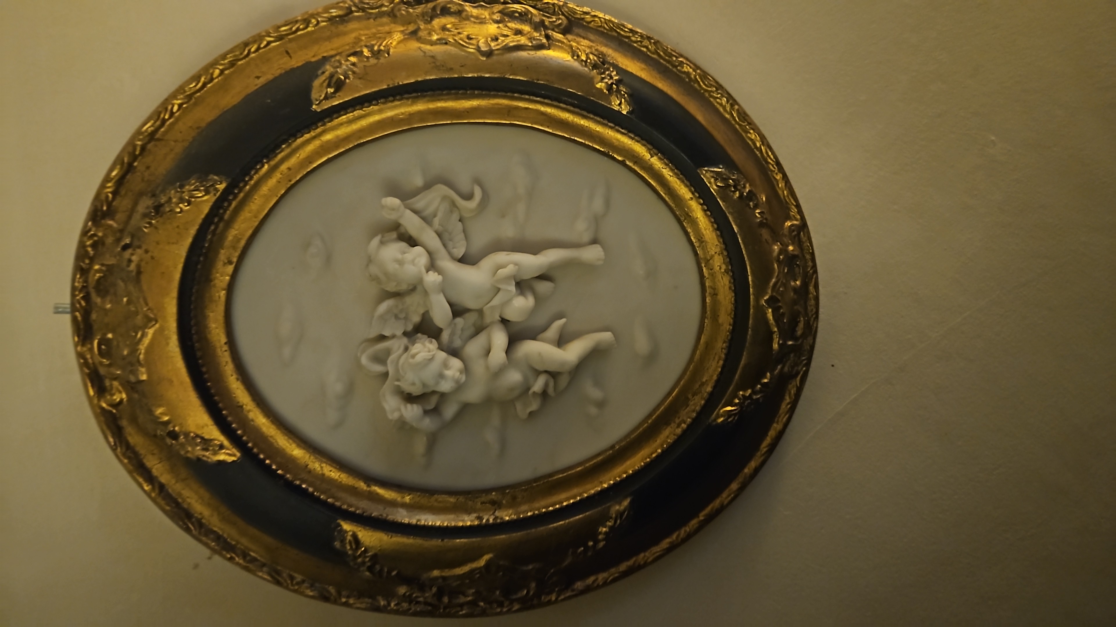 Médaillon ovale encadré de noir et d’or, orné de trois angelots blancs en relief