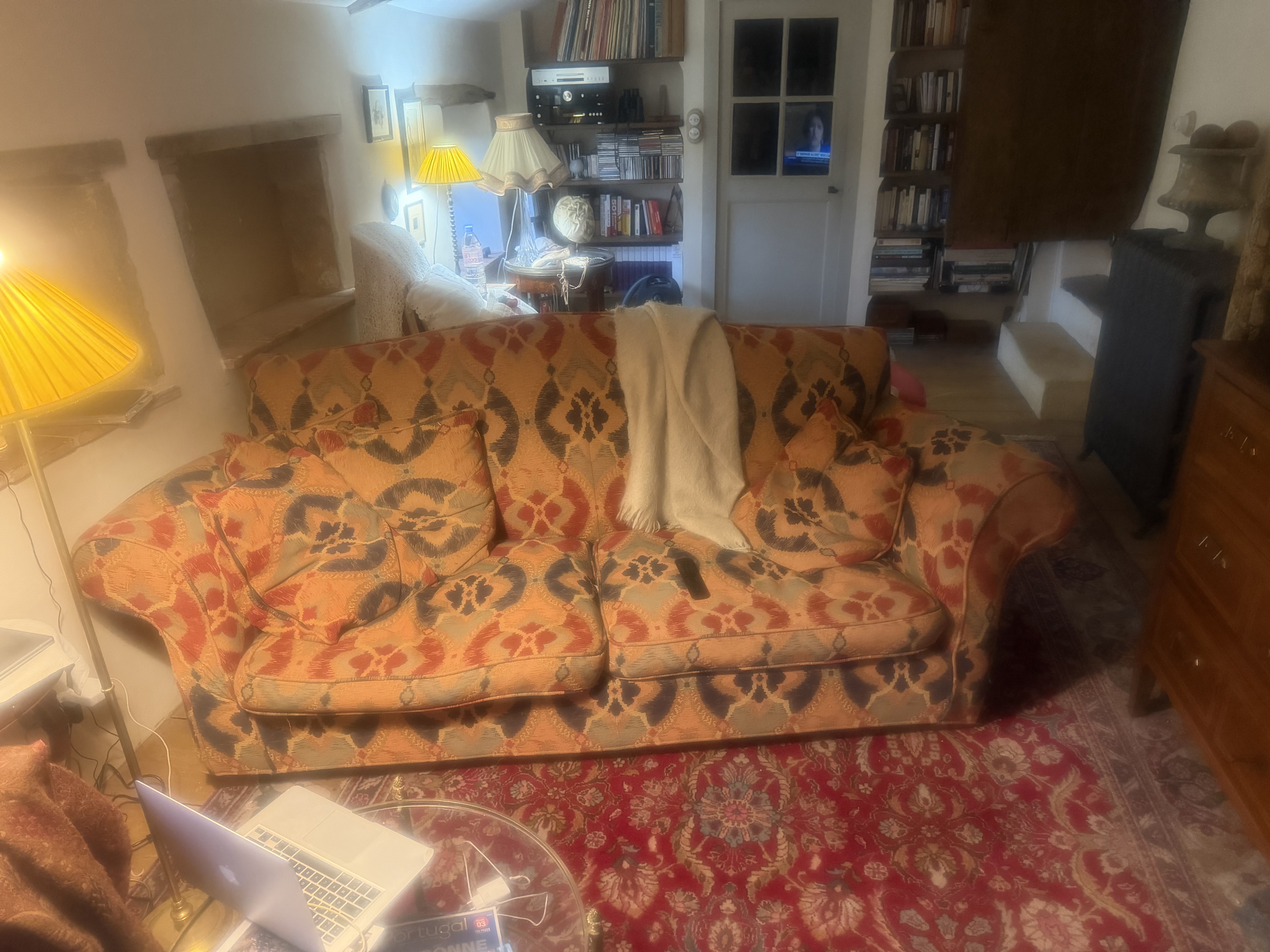 Canapé ancien recouvert d’un tissu rouge et ocre à larges motifs floraux