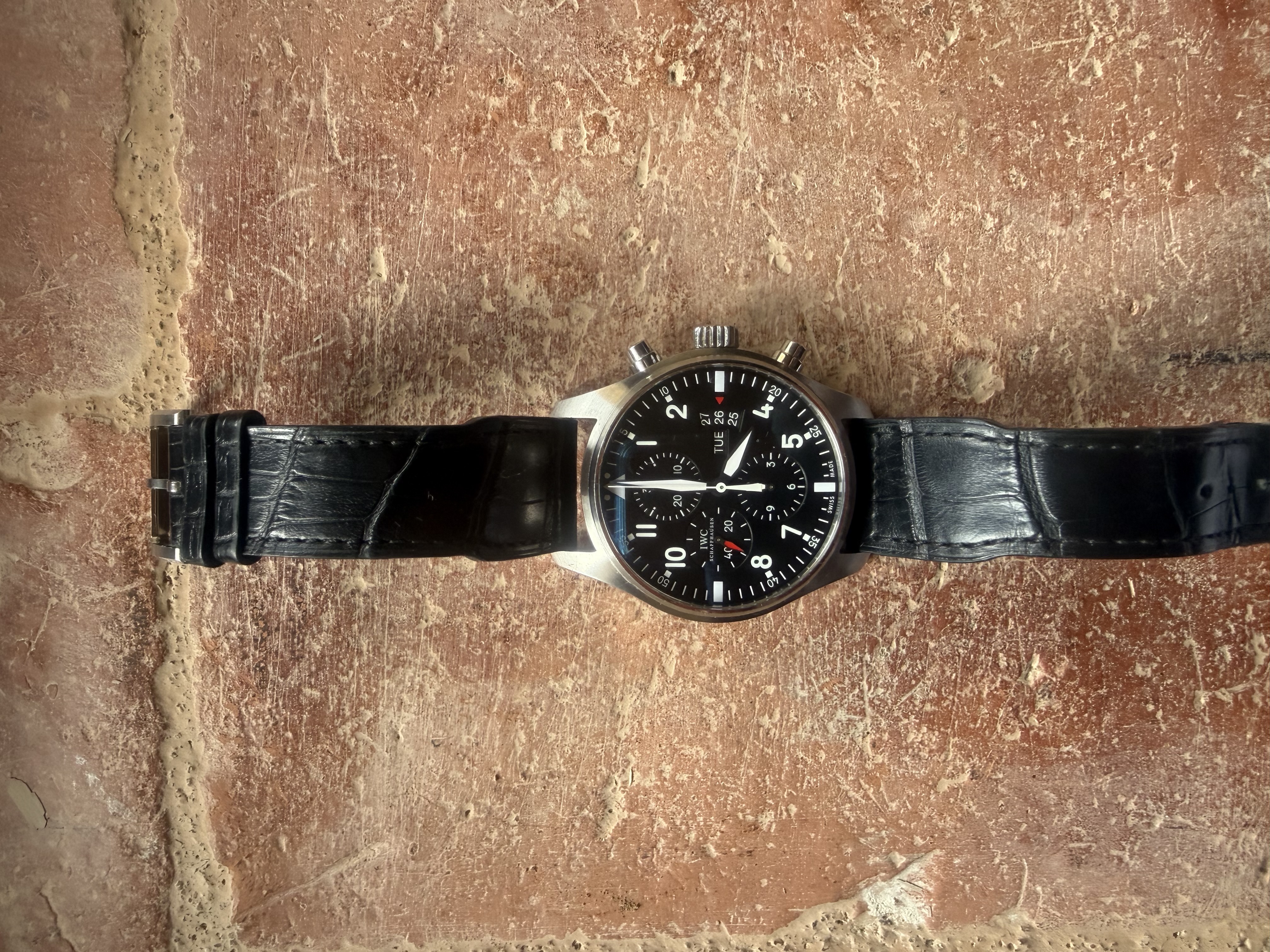 Montre noire à cadran sombre posée sur une surface de pierre rouge
